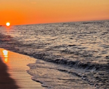 Słońce tuż nad horyzontem odbija się w mokrym piasku i morskich falach. Nasycone barwy pokazują urok zachod&oacute;w słońca na plaży w Jastarni.