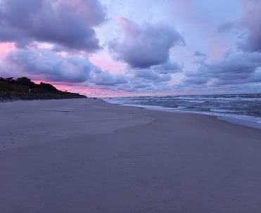 Plaża pod r&oacute;żowo-fioletowym niebem, z miękkim światłem i bardzo spokojną, pastelową atmosferą.