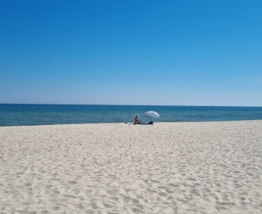 Szeroka, niemal pusta plaża i spokojne morze, z minimalistyczną kompozycją i letnim charakterem.